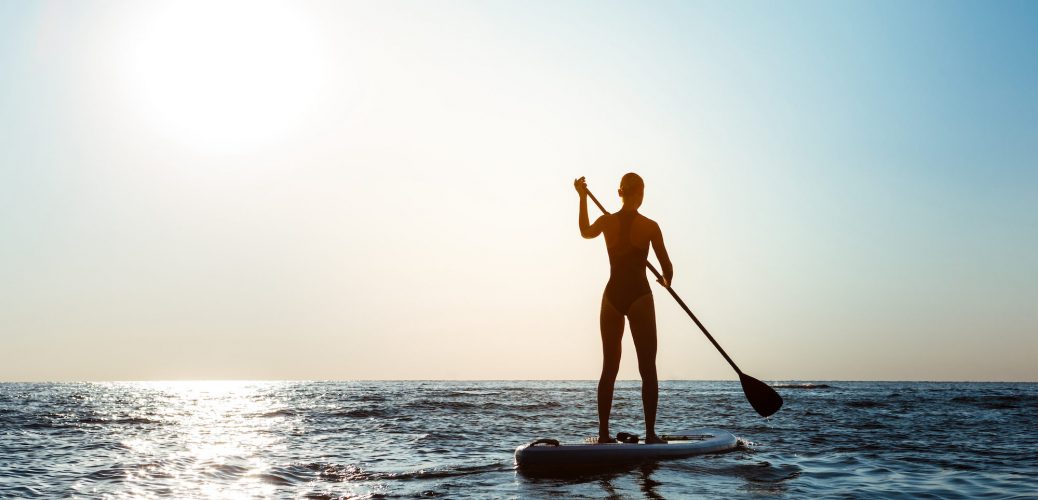 Silhouette of young beautiful girl surfing in sea at sunrise. Outdoors.
